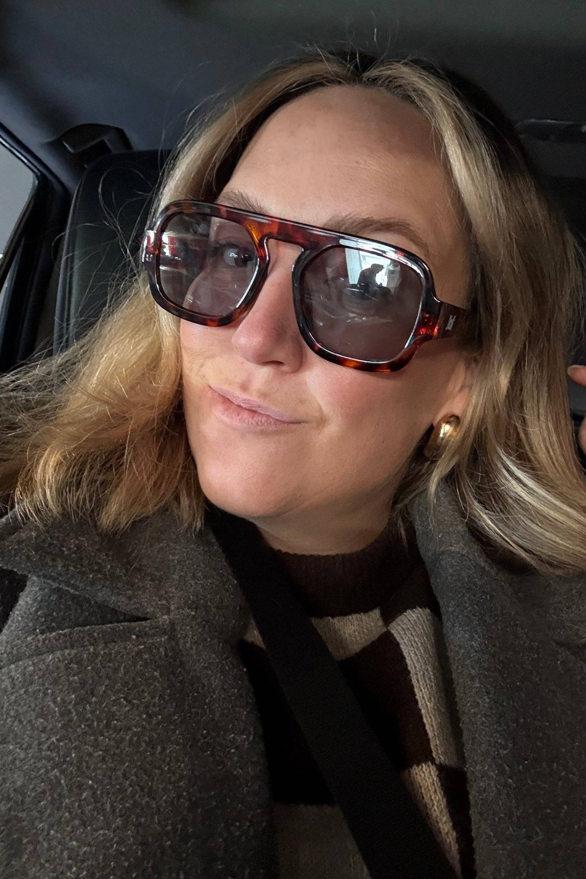 A woman wearing the Ella Sunglasses by Jenny Be Free, sitting in a car.