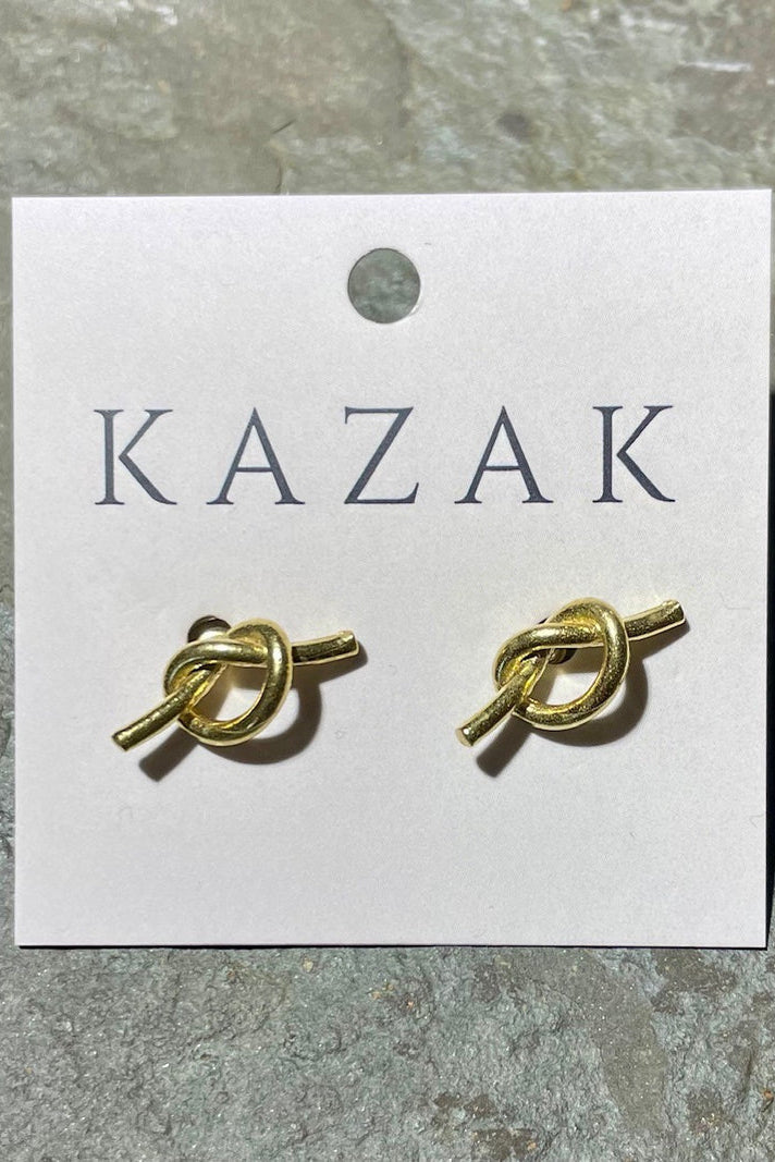 Brass knot earrings on a 'KAZAK' branded card against a stone background