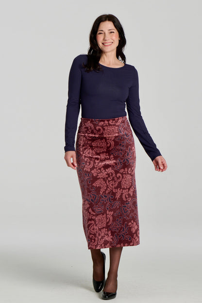 A woman wearing the Loretto Top by Kollontai in Navy, a slim fitting long sleeved top with a round neck. She is wearing it with the Winslet Skirt and standing in front of a grey background. 
