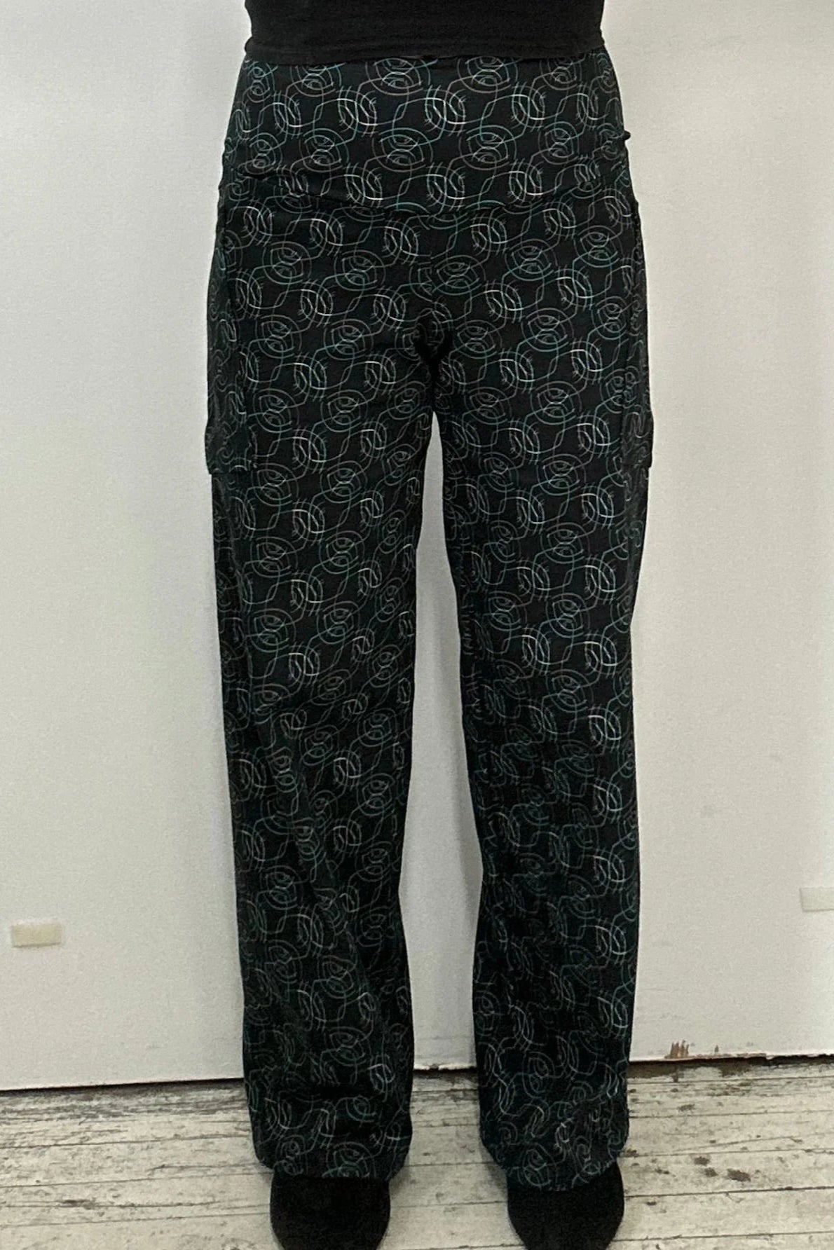 Waist down view of a woman wearing the Elma Pants by Kollontai in Turquoise on black print, straight legged pants with a wide elastic waist and large slant pockets. 