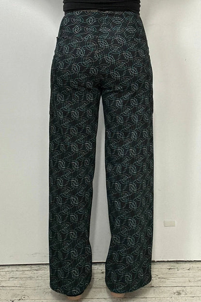 Back waist down view of a woman wearing the Elma Pants by Kollontai in Turquoise on black print, straight legged pants with a wide elastic waist and large slant pockets. 