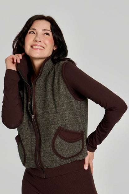 A woman wearing the Loretto Top by Kollontai in Chocolate, a slim fitting long sleeved top with a round neck. She is wearing it with a tweed vest and matching pants. 