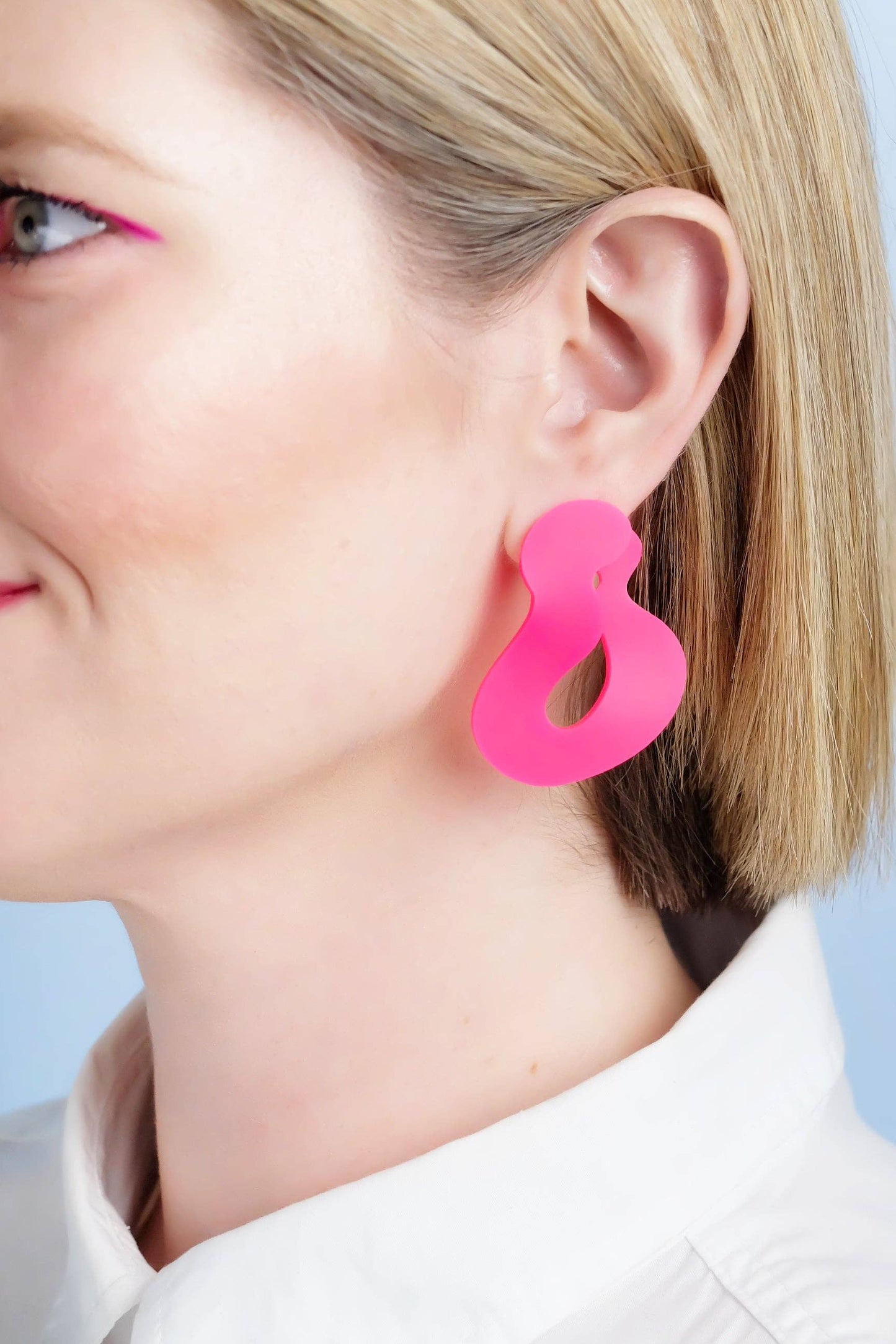 Close-up of a person wearing bright pink earrings against a light blue background