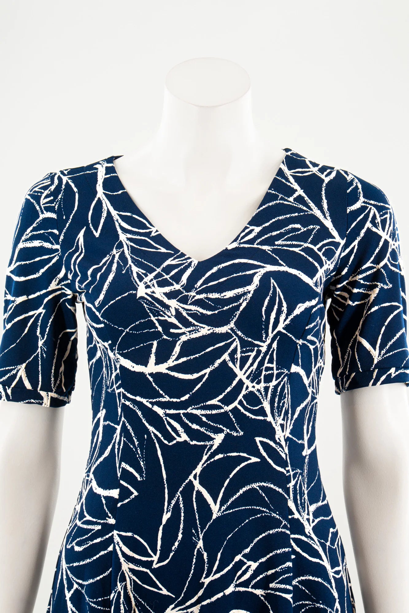 A close up view of the Liana Dress by Karkass in Navy and white print, an above the knee dress with short sleeves, a V-neck and princess seams, is show on a mannequin against a white background. 
