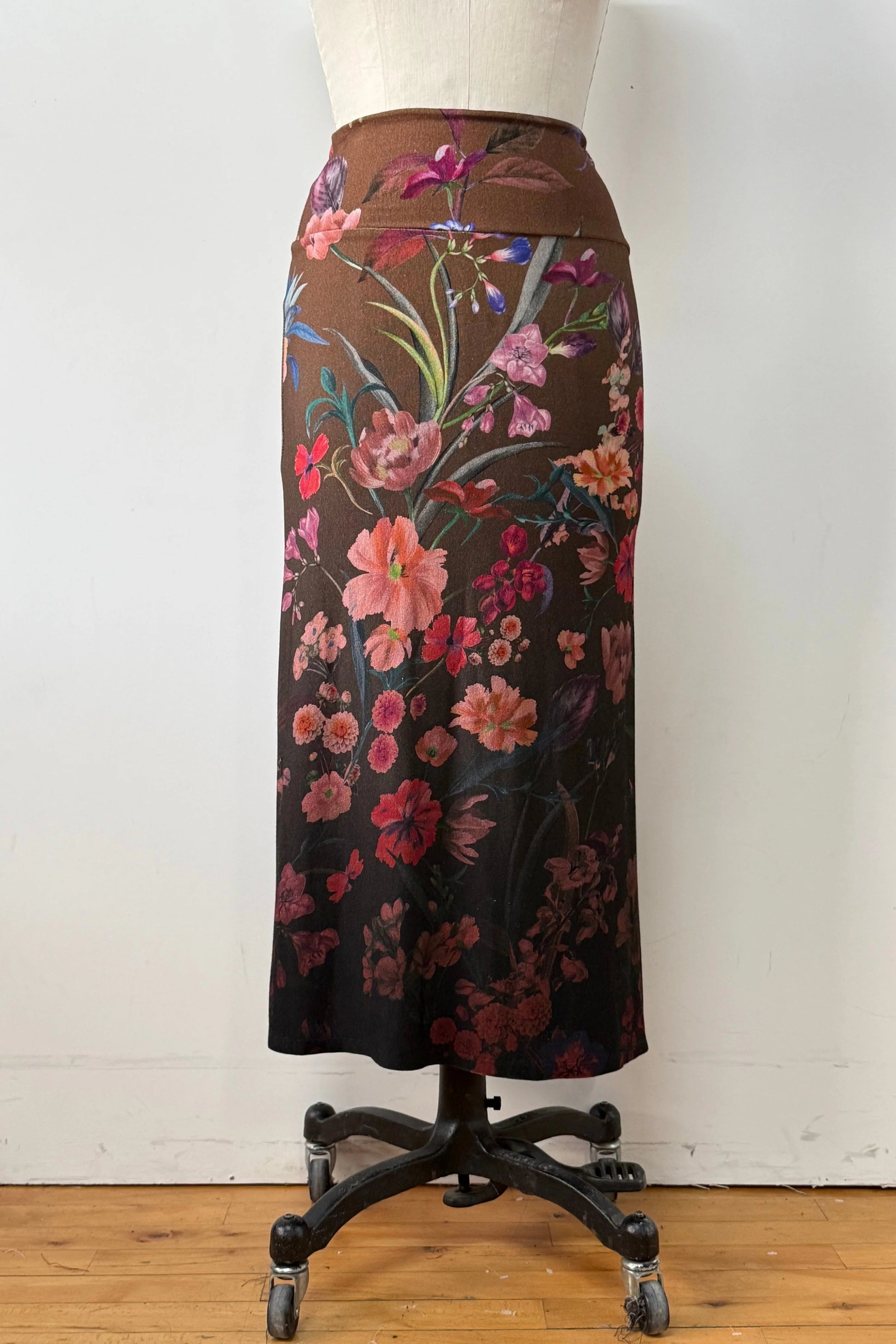 The Charlotte SKirt by Kollontai, a long slim cut brown skirt adorned with a floral pattern, is shown on a mannequin against a white background. 