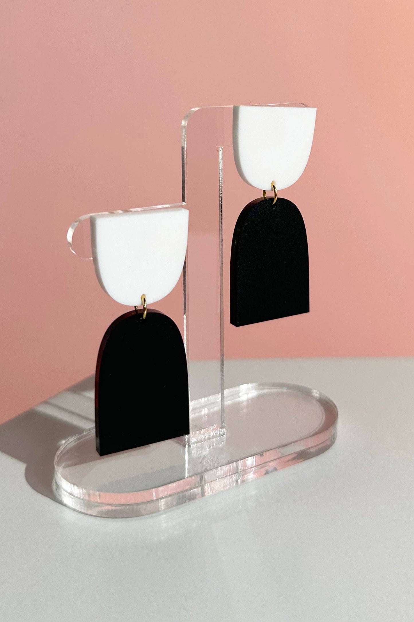 Black and white earrings on a clear stand against a pink background
