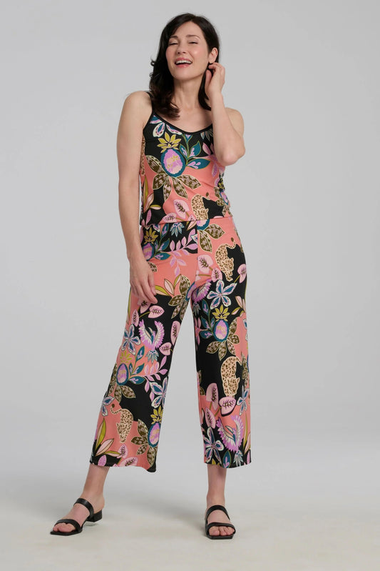 A woman wearing the Ortiga Jumpsuit by Kollontai, featuring a cheetah/floral print, spaghetti straps, an elastic waist, and 7/8 straight legs. She is standing in front of a grey background.