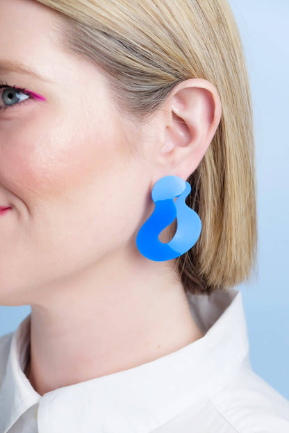 Blue earrings worn by a person against a light blue background