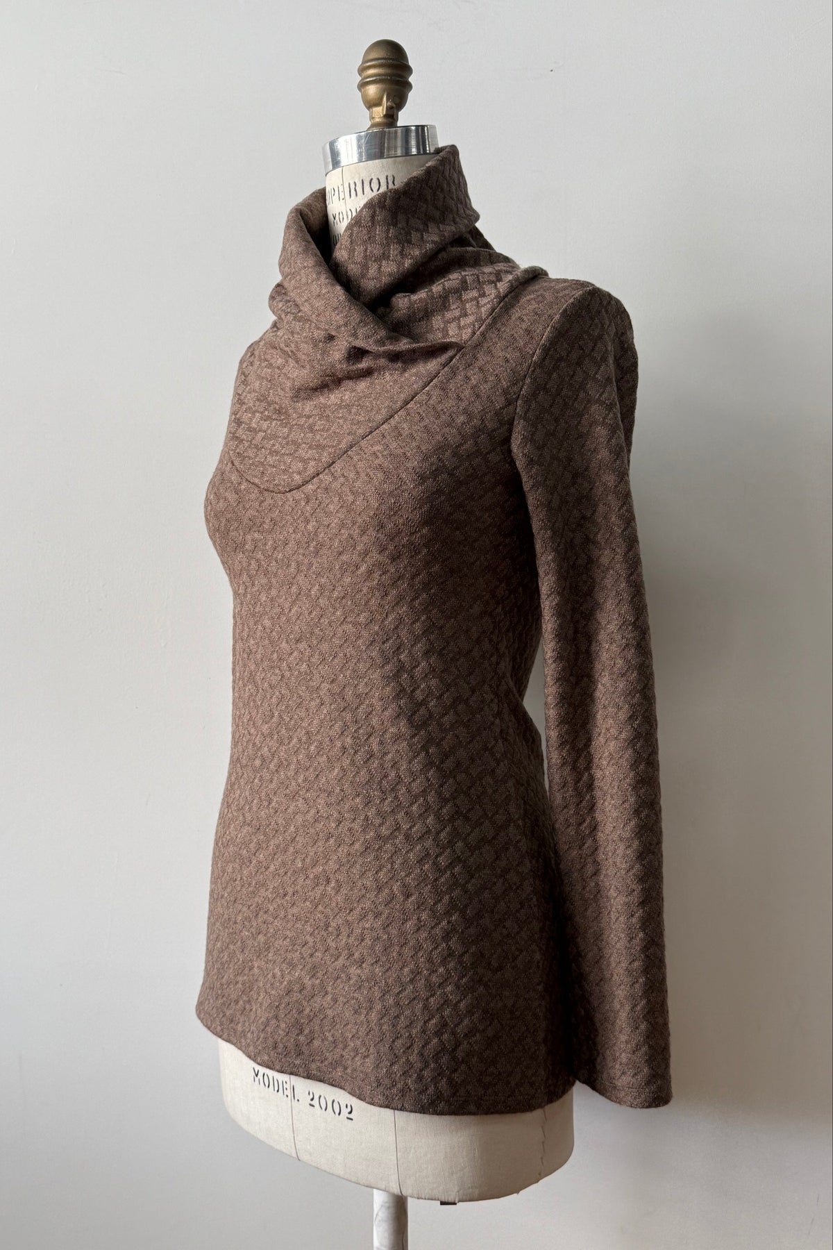 A side view of the Eloi Sweater by Kollontai in Brown, a slim fitting textured sweater with a large crossover collar, is shown on a mannequin against a white background.