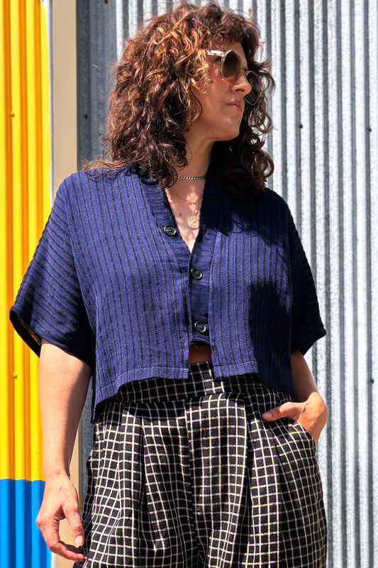 Woman wearing the Pip Jacket by Allison Wonderland in Navy/Black Stripe, with checkered pants standing against a colourful wall.