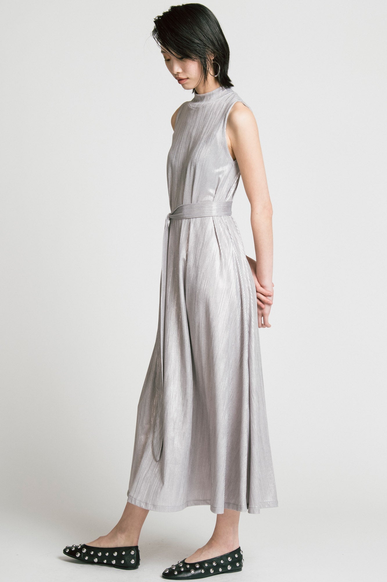 Side view of a woman wearing the Swing Dress by Allison Wonderland in Silver, a sleeveless mock neck maxi dress in shimmery fabric. 