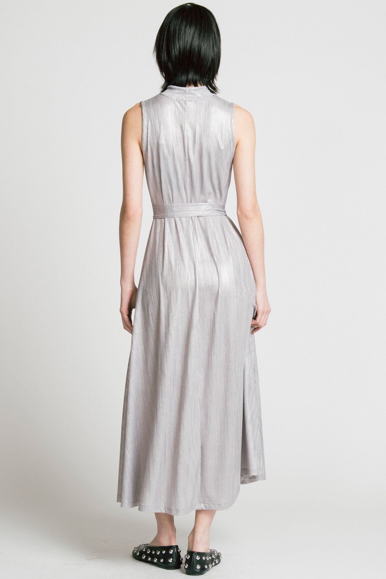 Back view of a woman wearing the Swing Dress by Allison Wonderland in Silver, a sleeveless mock neck maxi dress in shimmery fabric. 