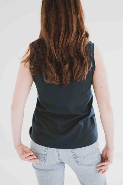 Back view of woman wearing the Riviera Tank by Ang Hill in Juniper, a loose fitting tank with a round neck and white straps in cotton/modal. She is wearing it with jeans and standing in front of a white background. 