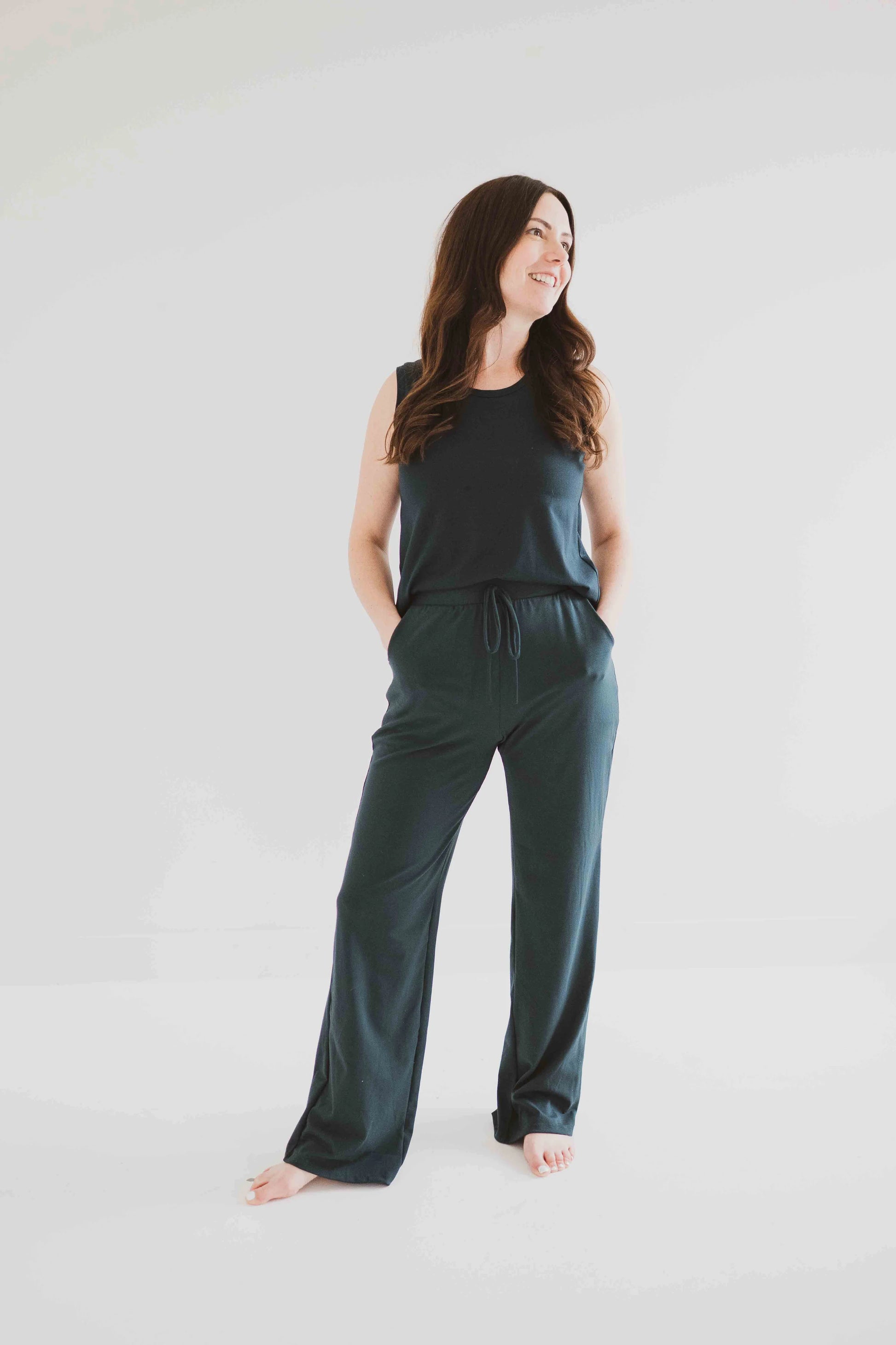 A woman wearing the Riviera Tank by Ang Hill in Juniper, a loose fitting tank with a round neck and white straps in cotton/modal. She is wearing it with matching pants and standing in front of a white background. 