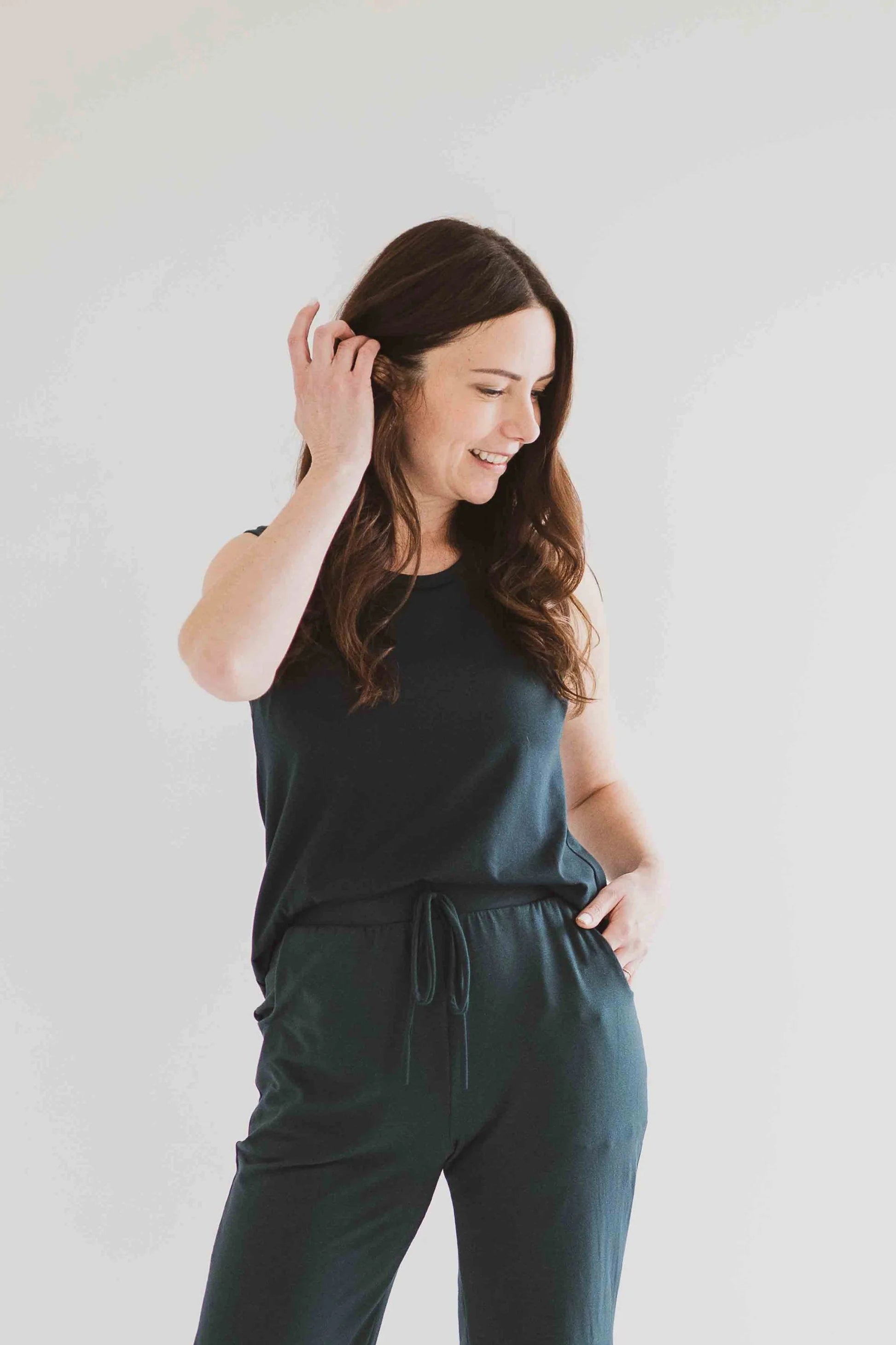 3/4 view of a woman wearing the Riviera Tank by Ang Hill in Juniper, a loose fitting tank with a round neck and white straps in cotton/modal. She is wearing it with matching pants and standing in front of a white background. 
