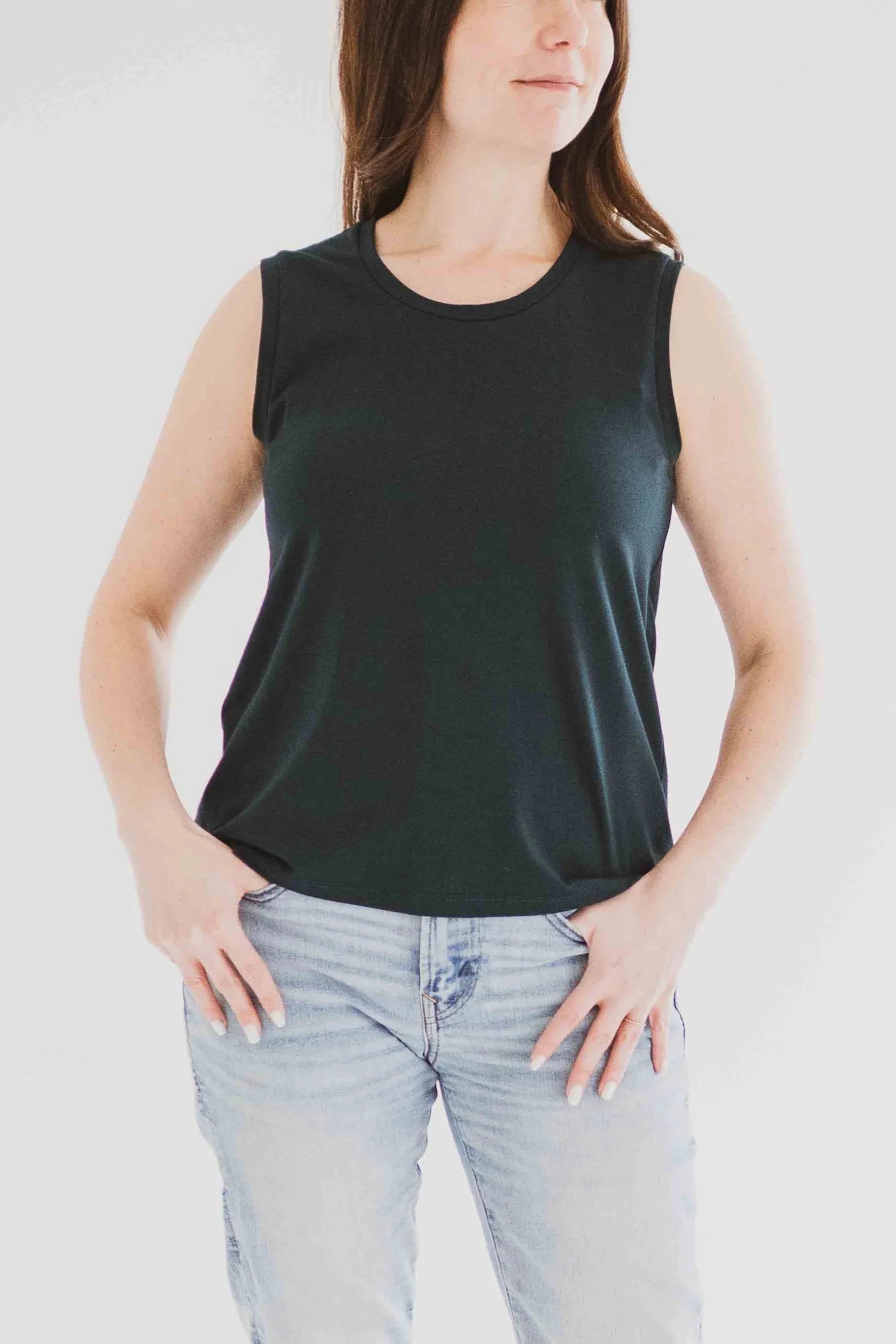 3/4 view of a woman wearing the Riviera Tank by Ang Hill in Juniper, a loose fitting tank with a round neck and white straps in cotton/modal. She is wearing it with jeans and standing in front of a white background. 