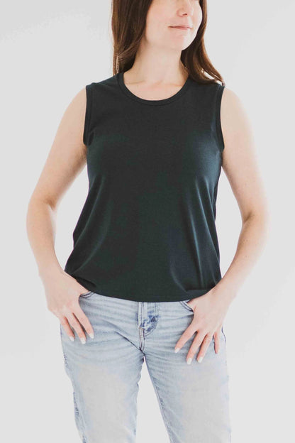 3/4 view of a woman wearing the Riviera Tank by Ang Hill in Juniper, a loose fitting tank with a round neck and white straps in cotton/modal. She is wearing it with jeans and standing in front of a white background. 