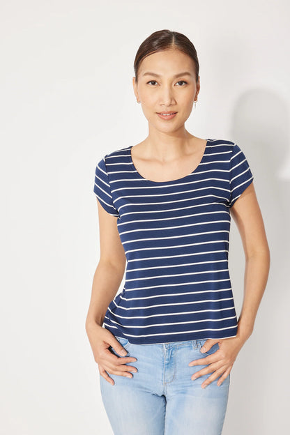 A woman wearing the Fjord T-shirt by Canopée in Navy/White stripe, a short-sleeved tee with a wide scooped neck and a slightly loose fit. She is wearing it with jeans and standing in front of a white background. 