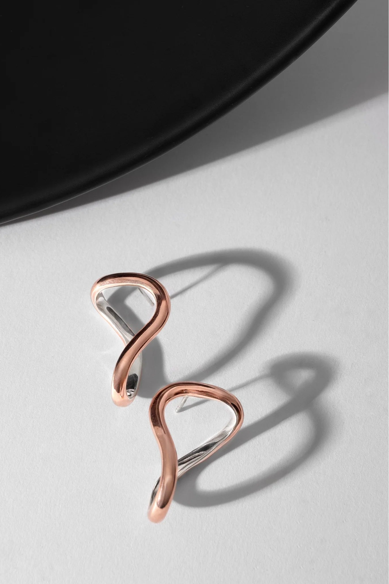 Silver lined copper earrings on a light gray surface with a black plate in the background