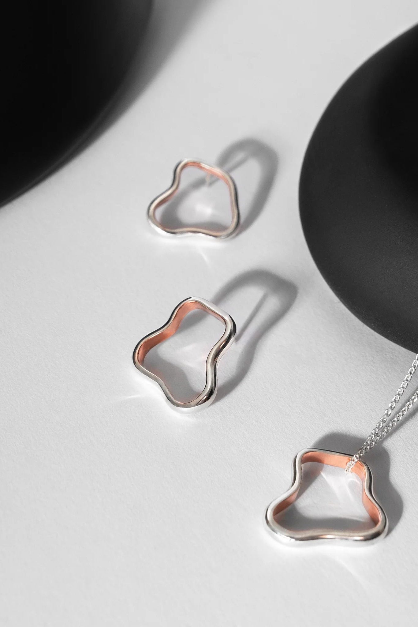 Copper lined silver stud earrings and necklace on a light gray background