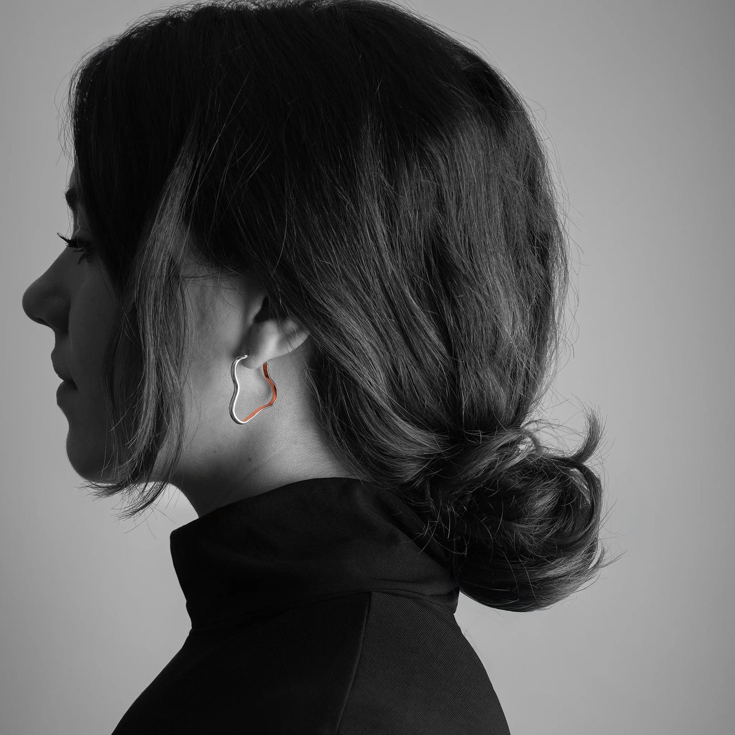 Side profile of a person with styled hair and earrings on a plain background