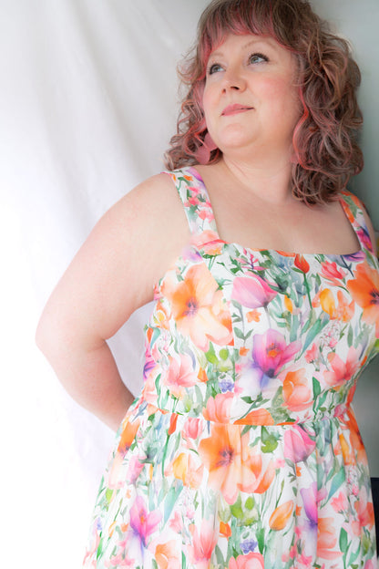 A woman wearing the Rue Floral Dress by Compli K, a midi-length tank dress with wide straps, a square neckline, a gathered waist and a full skirt. She is shown against a white background.