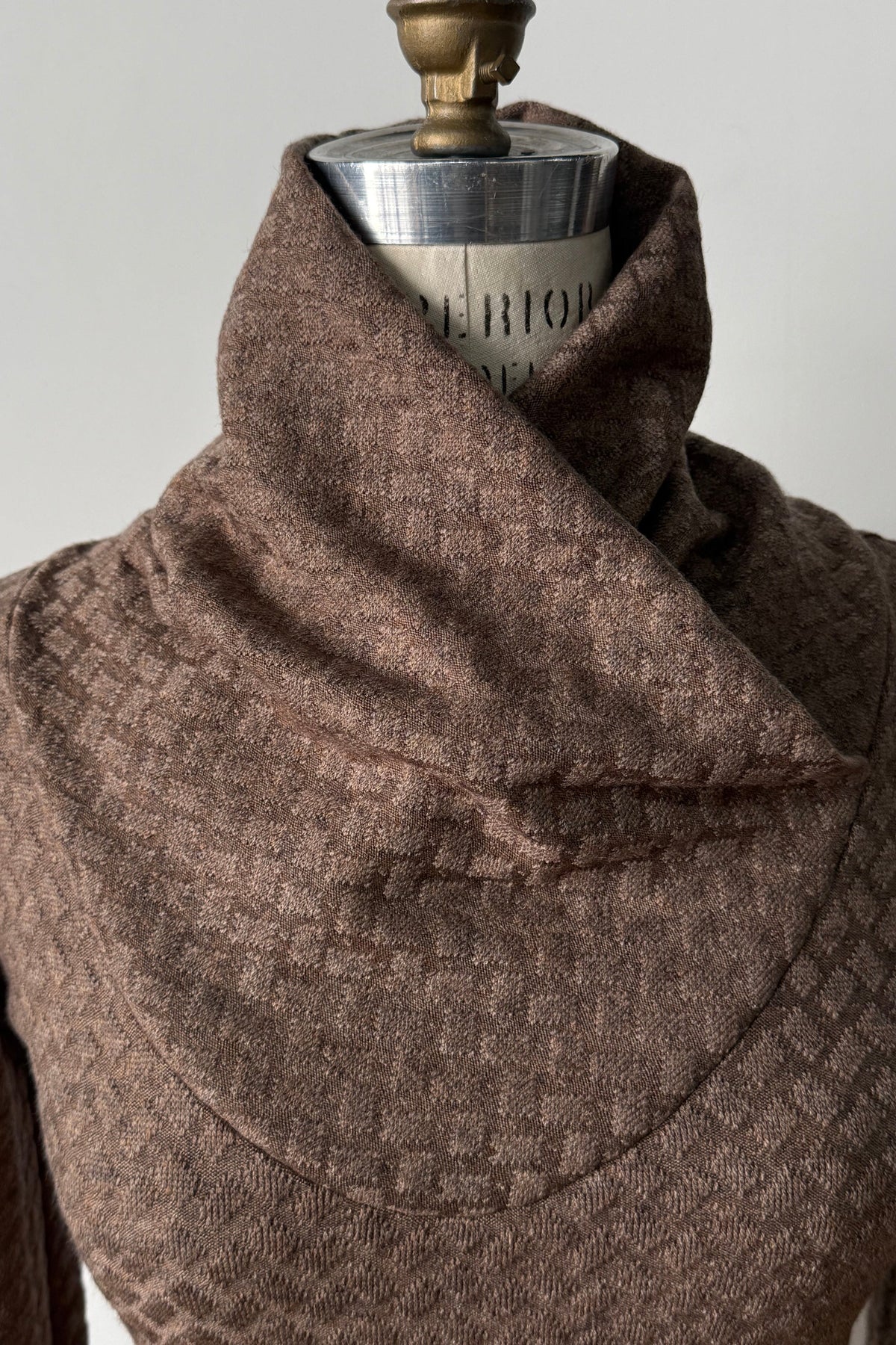 A close up of the Eloi Sweater by Kollontai in Brown, a slim fitting textured sweater with a large crossover collar, is shown on a mannequin against a white background.