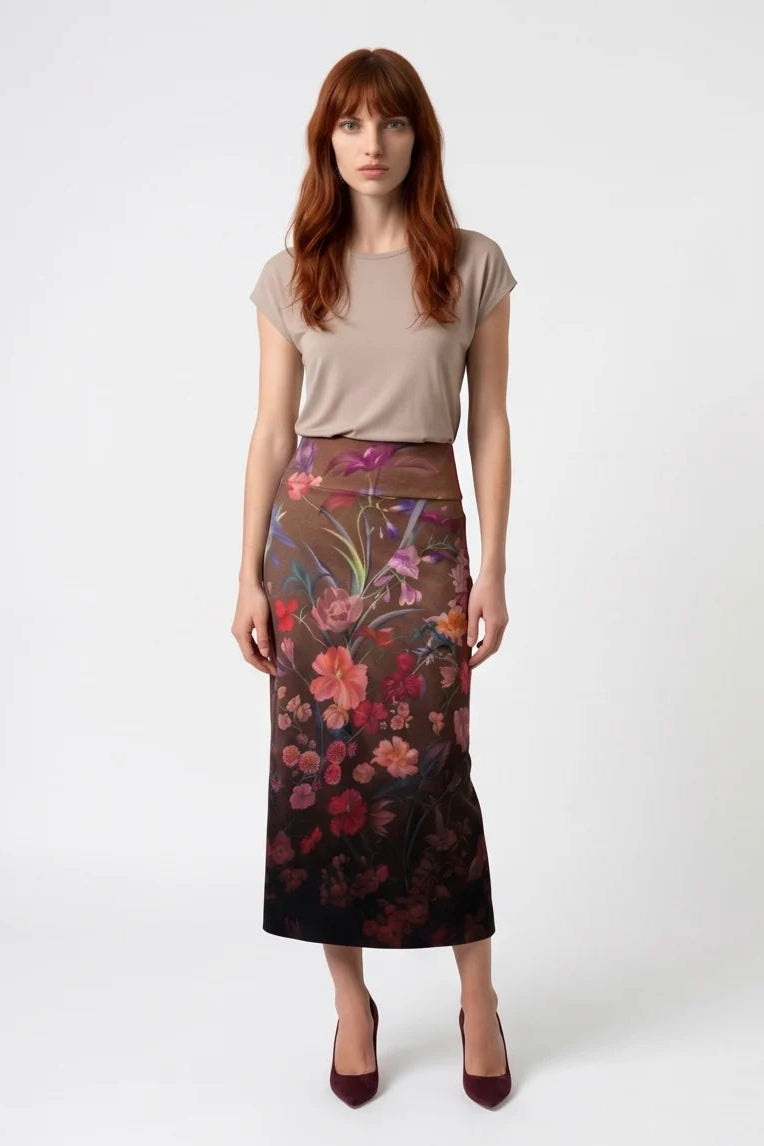 A woman wearing the Charlotte SKirt by Kollontai, a long slim cut brown skirt adorned with a floral pattern. She is wearing it with a beige top against a white background