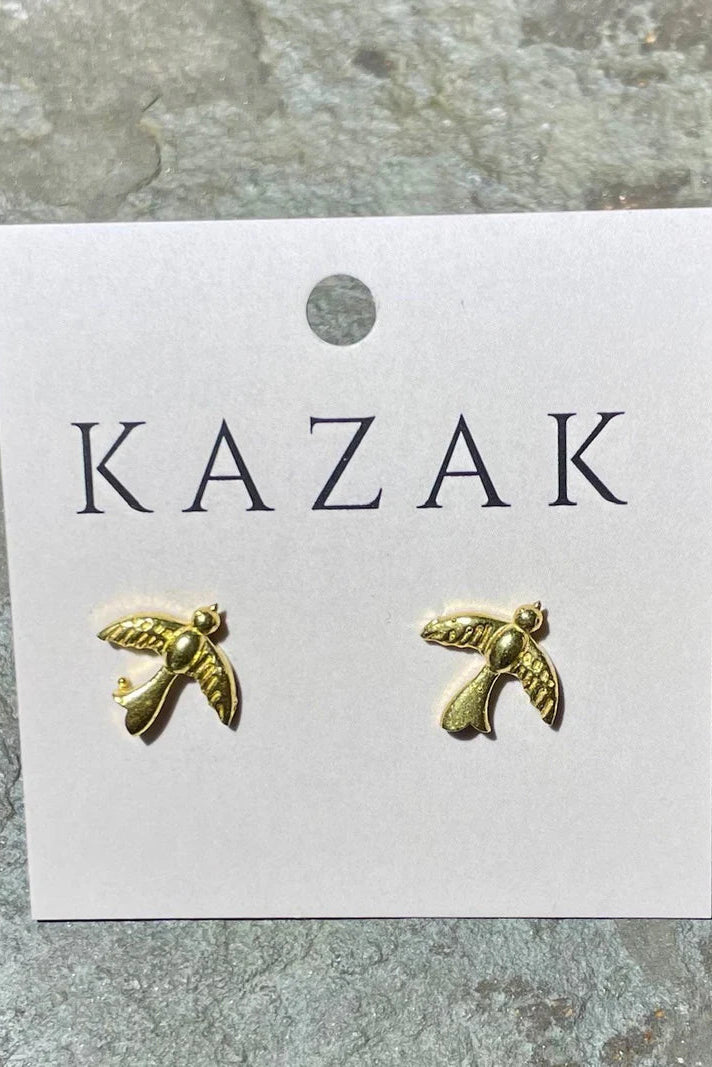 Brass Swallow-shaped earrings on a 'KAZAK' branded card against a stone background