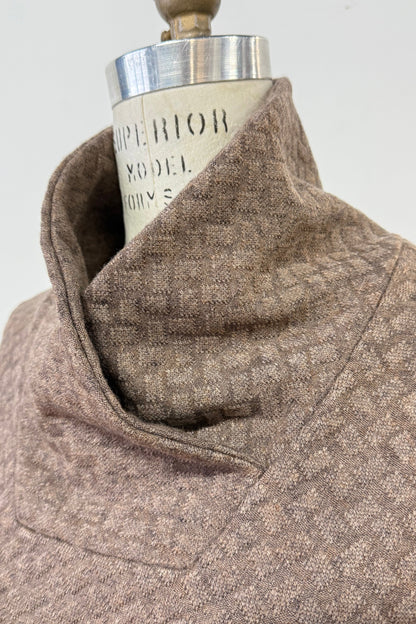 A close up of the collar of the Sacha Tunic by Kollontai in Brown, a textured knit straight cut tunic with a funnel collar and large patch pockets, is shown on a mannequin against a white background. 