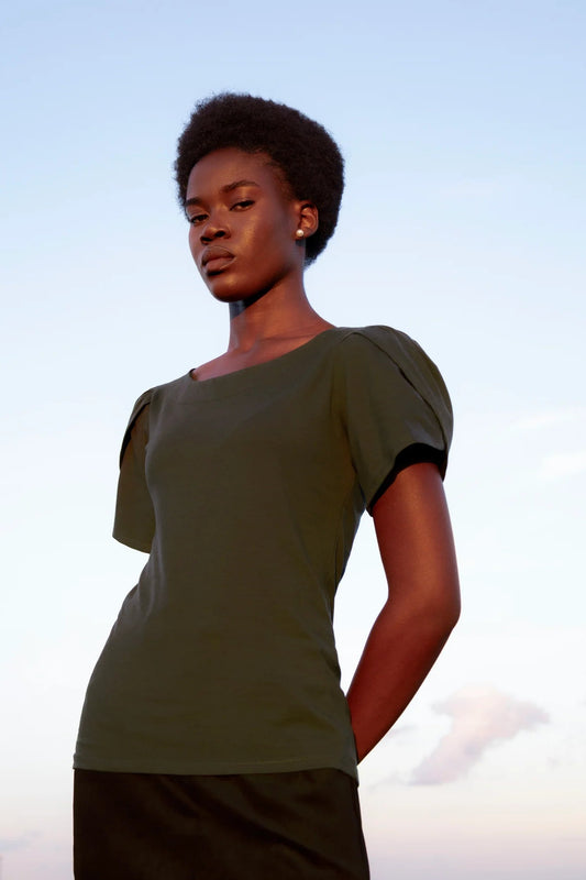 A woman wearing the Tanzania Tulip Top by Eve Lavoie in Green, with a round neck and tulip sleeves. She is standing outdoors against a soft blue sky.
