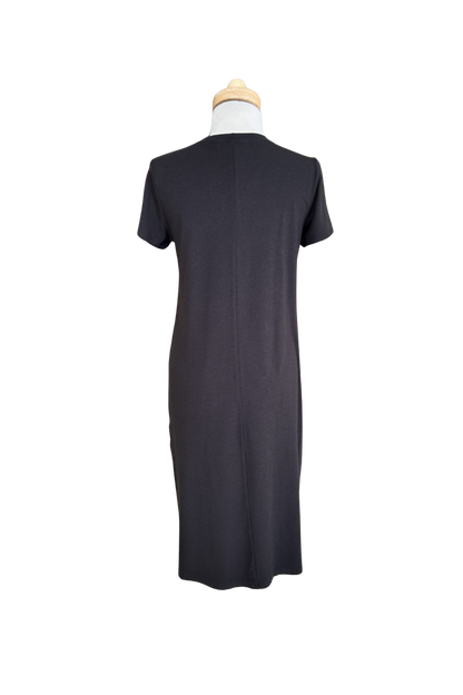 A back view of the Frances Midi  by Tangente in Black, a short sleeved loose fitting dress with side slits, is shown on a mannequin against a white background. 