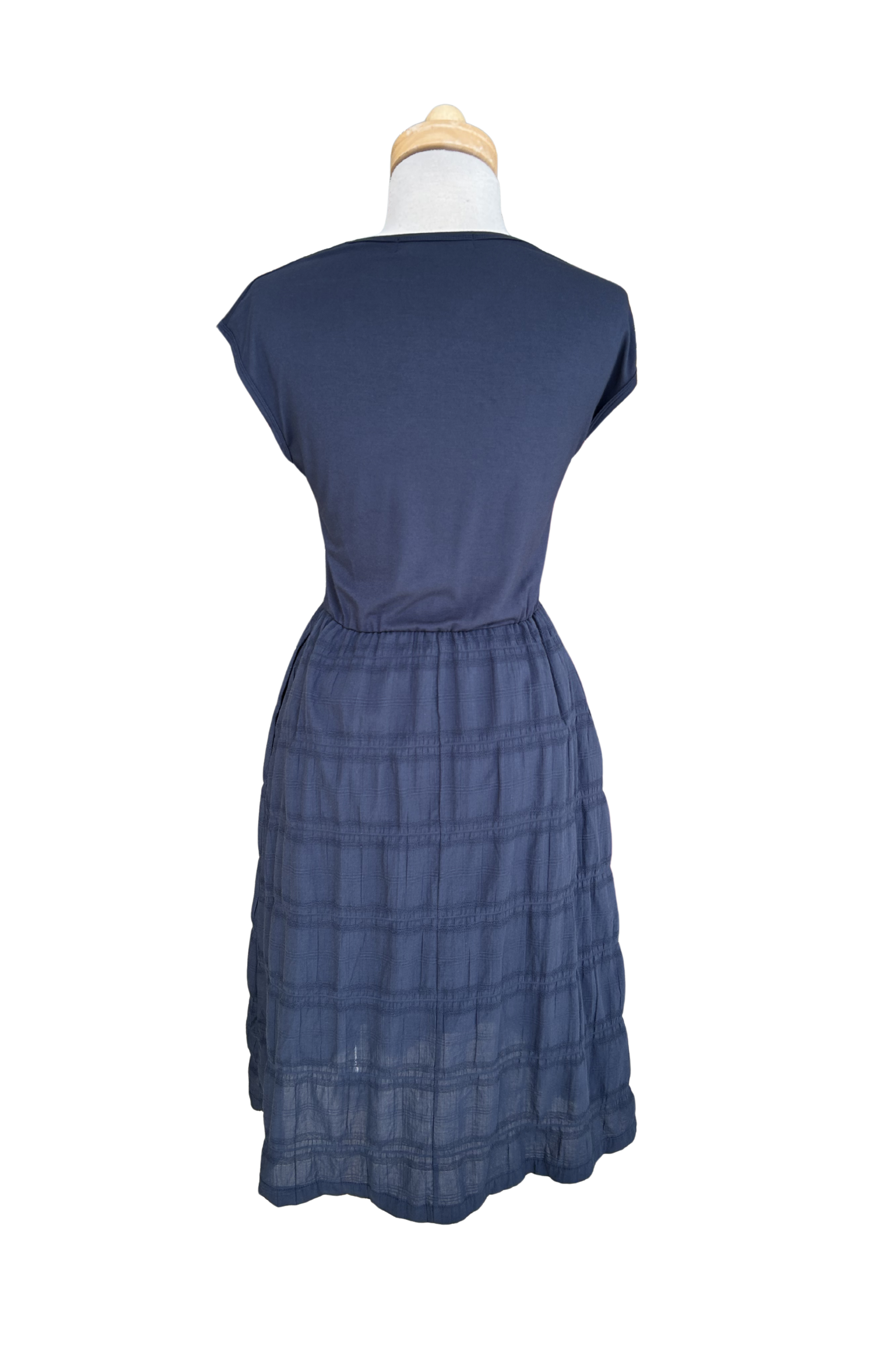 A back view of the Mona Dress by Tangente in Navy, a below the knee length dress featuring a bamboo rayon bodice and seersucker skirt, with short sleeves and a round neck, is shown on a mannequin against a white background. 