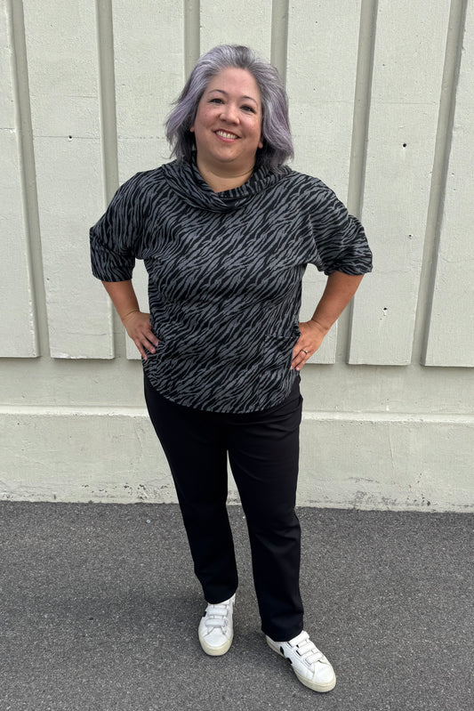A woman wearing the Francis Tunic by Pure in Black/Charcoal animal print, featuring a turtleneck, 3/4 sleeves and two patch pockets. She is wearing it with Black pants and standing in front of a grey wall. 