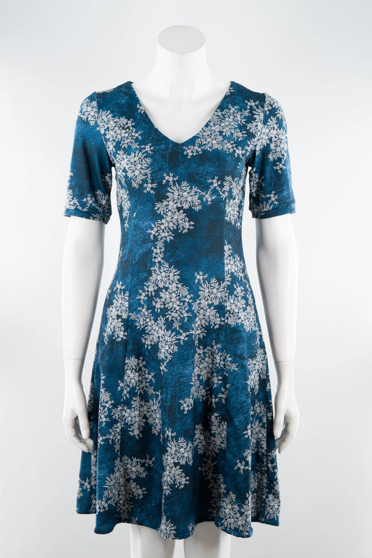 The Ice Flower Dress by Karkass in Blue Floral, a knit dress with a V-neck, elbow length sleeves, fit and flare shape, and above the knee hem, is shown on a mannequin in front of a white background. 