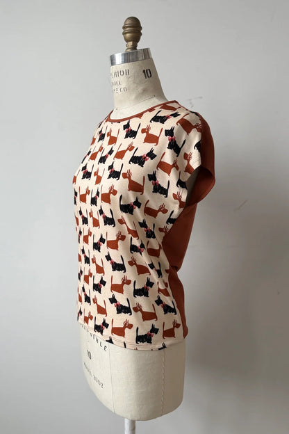 A side view of the Arty T-Shirt by Kollontai in Dogs/Rust print, with a round neck, short extended sleeves, and a slight hi-low hemline, and a solid rust back, is shown on a mannequin against a grey background. 