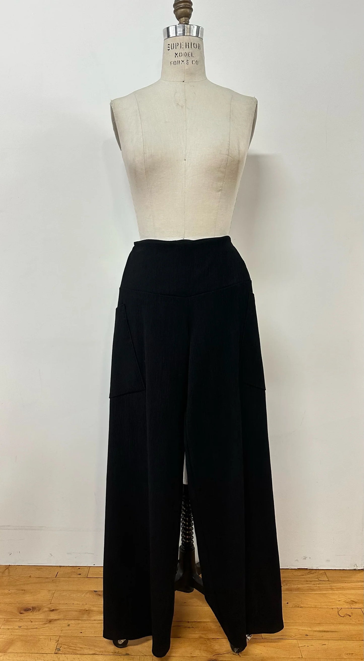 The Hermione Pants by Kollontai in Navy, stretchy corduroy pants with a wide pull-one waistband, wide legs, and angled patch pockets, are shown on a mannequin in front of a white wall. 