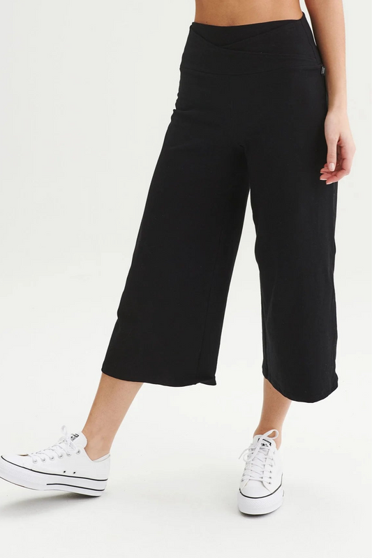 Waist down view of a woman wearing the Calla Capri by Message Factory in Black, wide leg cropped pants with a pull-on waistband that has a crossover detail, on a white background. 