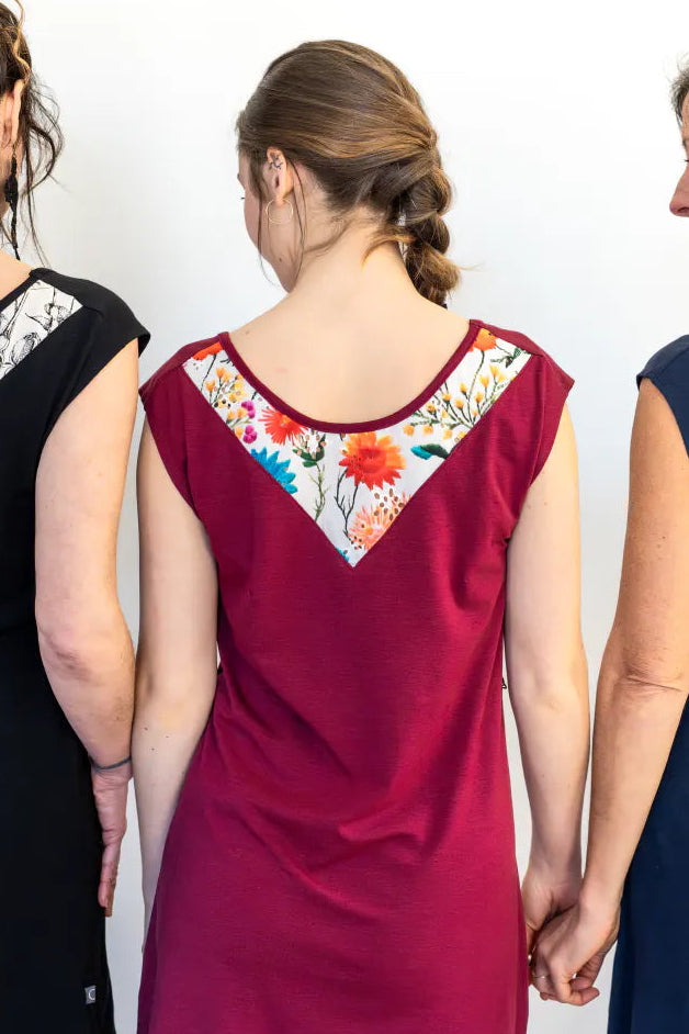 Back view of three woman wearing the Mariposa Dress by Marie C, a short sleeved short dress that's reversible back to front with printed yoke on one side, and an attached tie belt. The one in the centre is wearing it in Raspberry. 