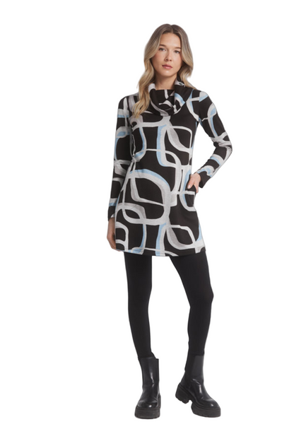 A woman wearing the Eve Tunic by Dinh Ba in Blue geometric print, a long sleeved tunic with a large cowl neck and an A-line shape. She is standing in front of a grey background. 