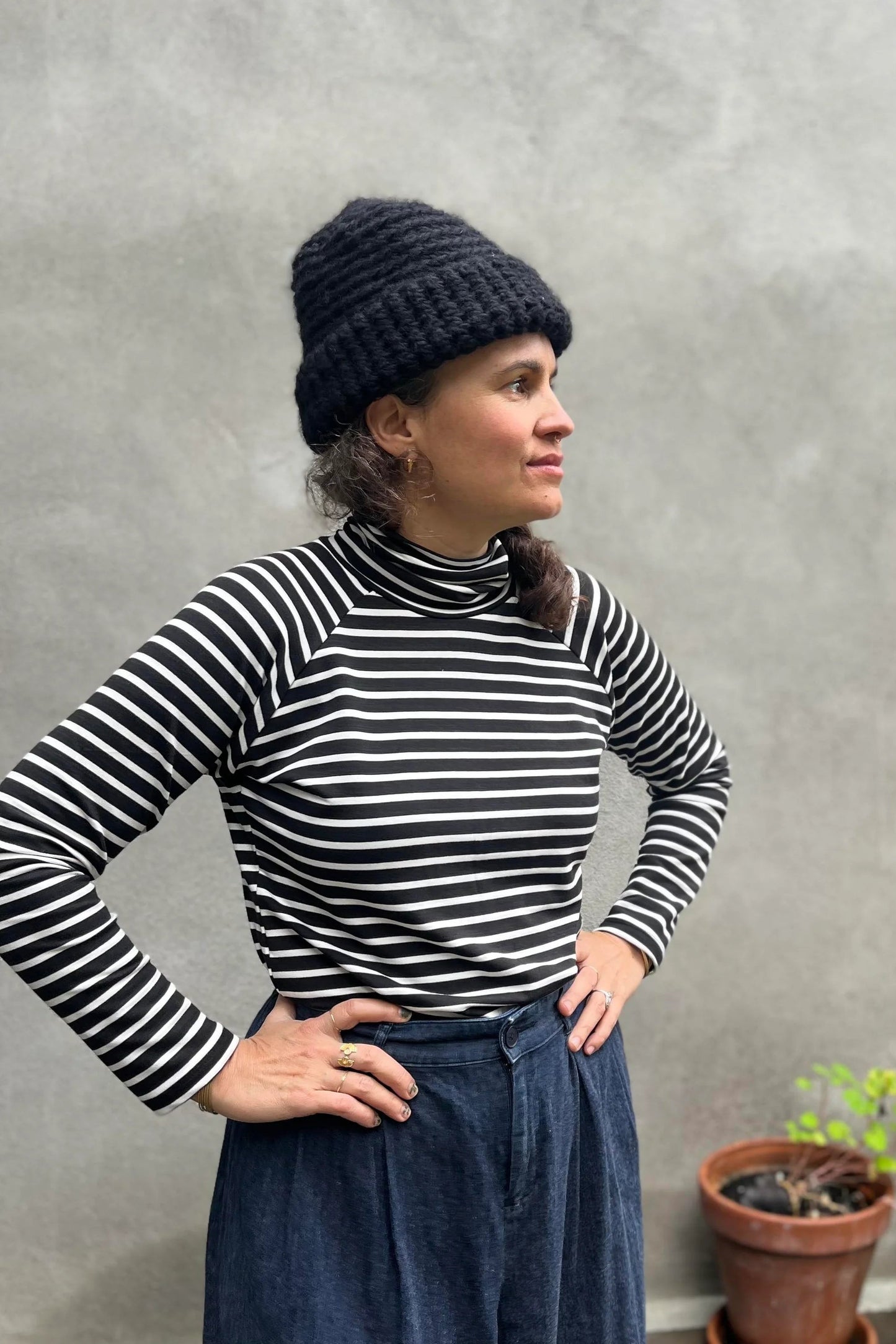 A woman wearing the Oris Raglan Turtleneck by Kazak in Black Stripe. She is wearing it with jeans and standing outside. 