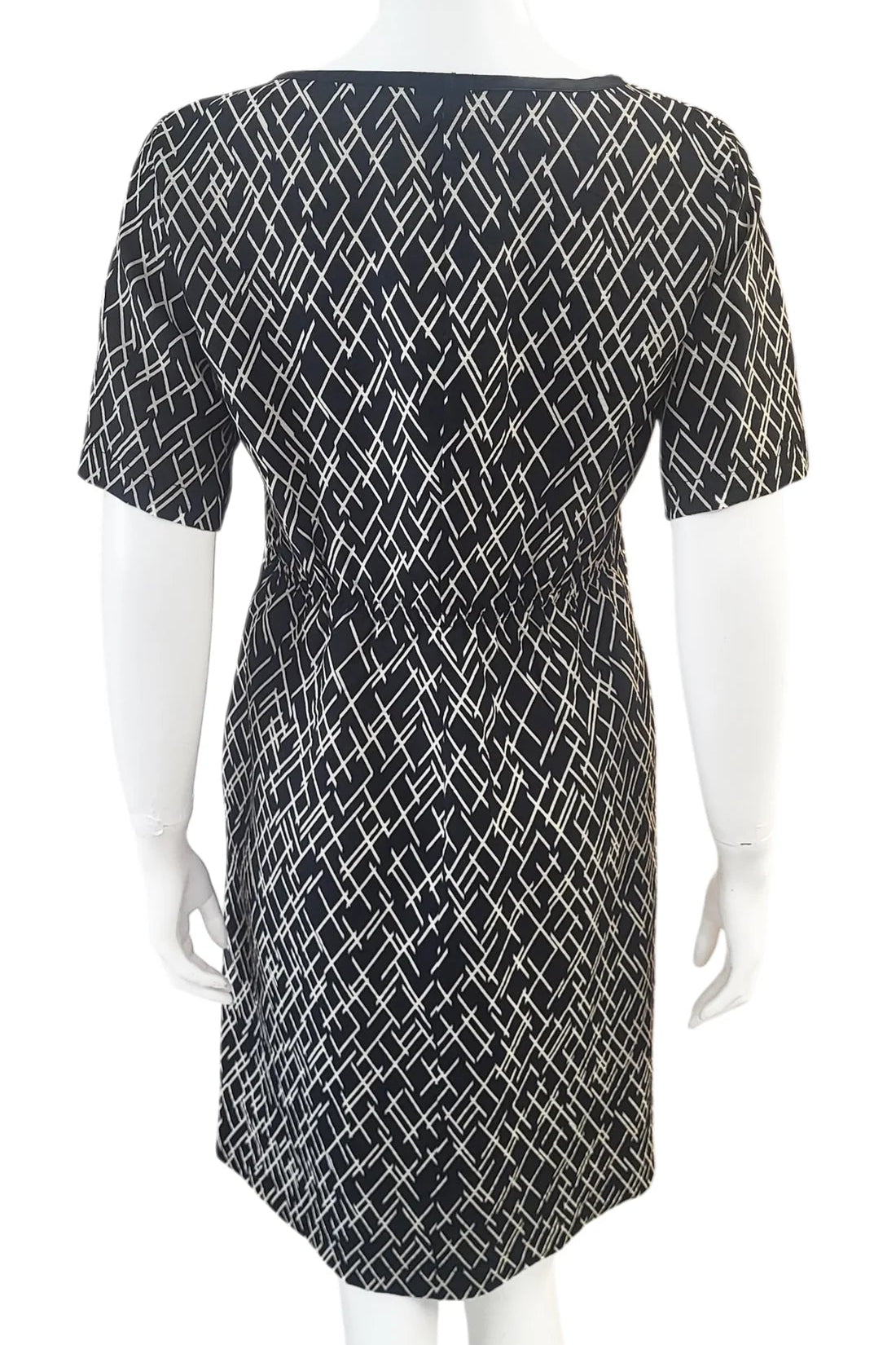 A back view of the Cecily Simple Shift Dress from Mandala in Crosstown print is shown on a mannequin against a white background. It has a high neck, short sleeves, a knee-length hem, French darts, and elastic at the back of the waist. 