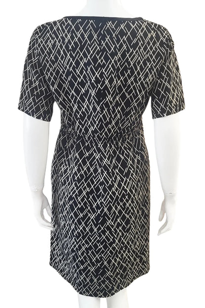 A back view of the Cecily Simple Shift Dress from Mandala in Crosstown print is shown on a mannequin against a white background. It has a high neck, short sleeves, a knee-length hem, French darts, and elastic at the back of the waist. 