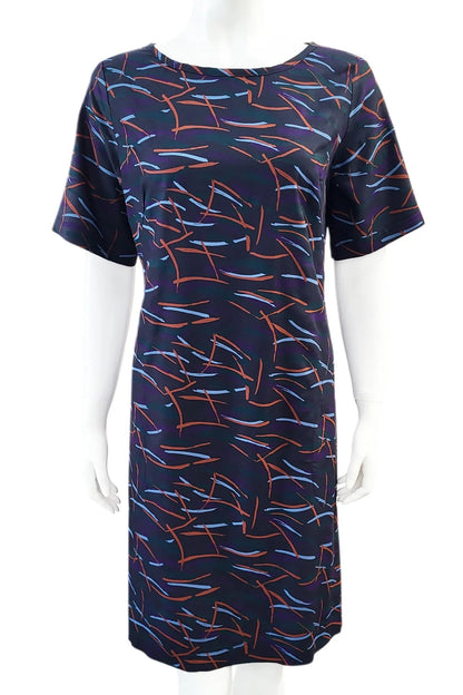 The Cecily Simple Shift Dress from Mandala in Dark Stix print is shown on a mannequin against a white background. It has a high neck, short sleeves, a knee-length hem, French darts, and elastic at the back of the waist. 