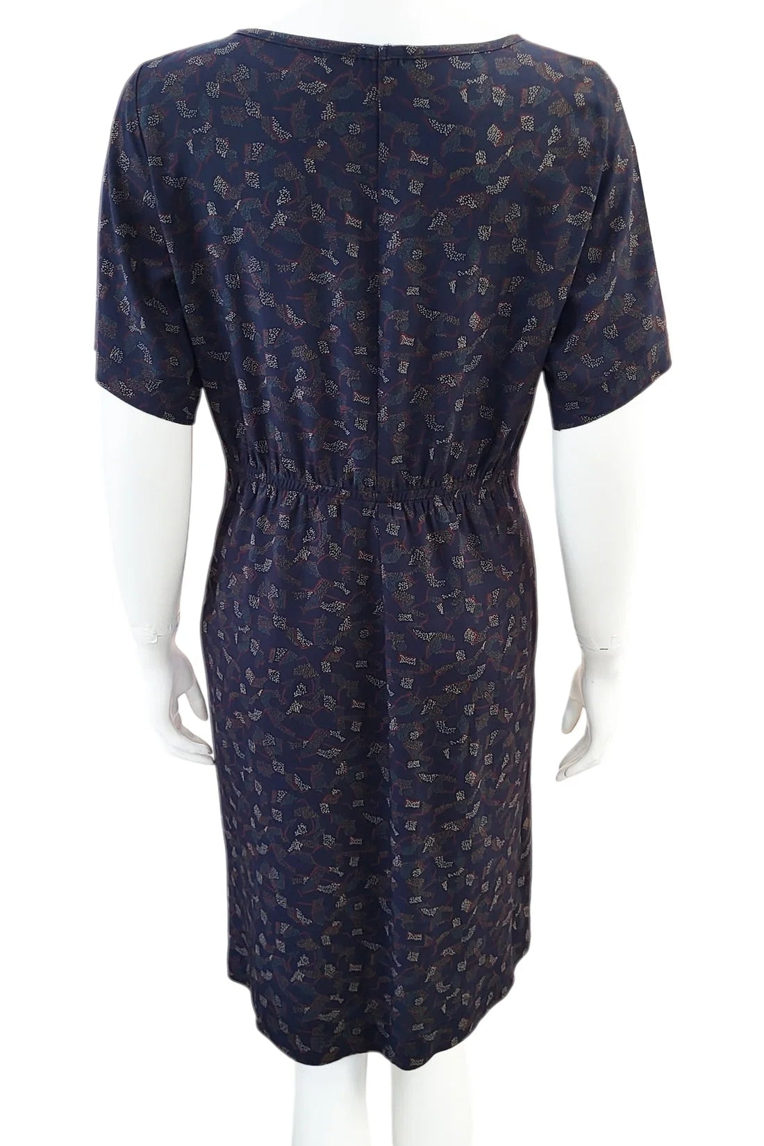 A back view of the Cecily Simple Shift Dress from Mandala in Night Hex print is shown on a mannequin against a white background. It has a high neck, short sleeves, a knee-length hem, French darts, and elastic at the back of the waist. 