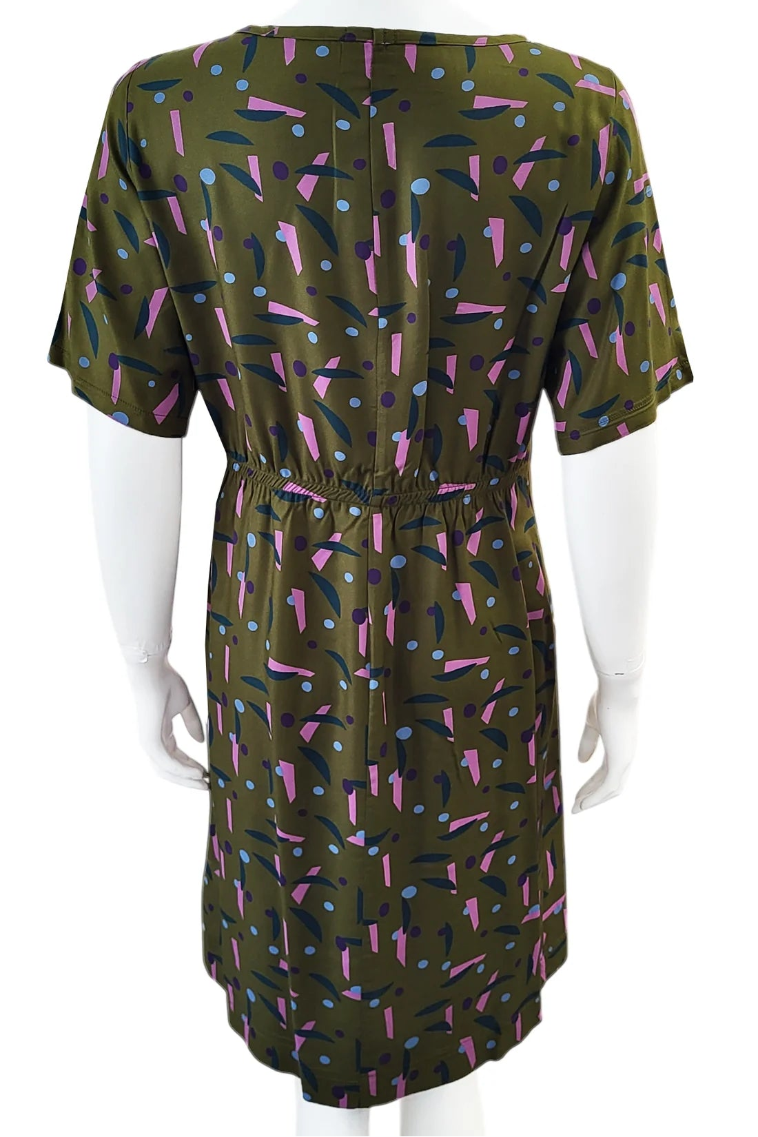 A back view of the Cecily Simple Shift Dress from Mandala in Playtime Ivy print is shown on a mannequin against a white background. It has a high neck, short sleeves, a knee-length hem, French darts, and elastic at the back of the waist. 