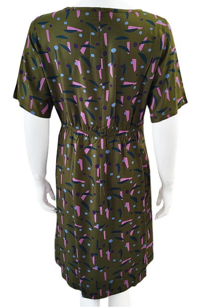 A back view of the Cecily Simple Shift Dress from Mandala in Playtime Ivy print is shown on a mannequin against a white background. It has a high neck, short sleeves, a knee-length hem, French darts, and elastic at the back of the waist. 