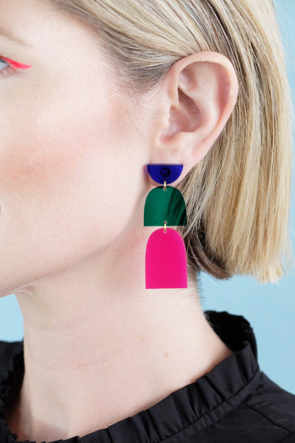 Close-up of a person wearing colorful geometric earrings against a light blue background