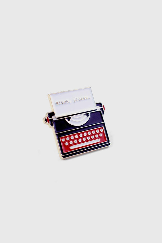 The Typewriter Pin by Badaboöm Studio, featuring a red typewriter and white paper that reads "Bitch, Please" is shown against a white background. 