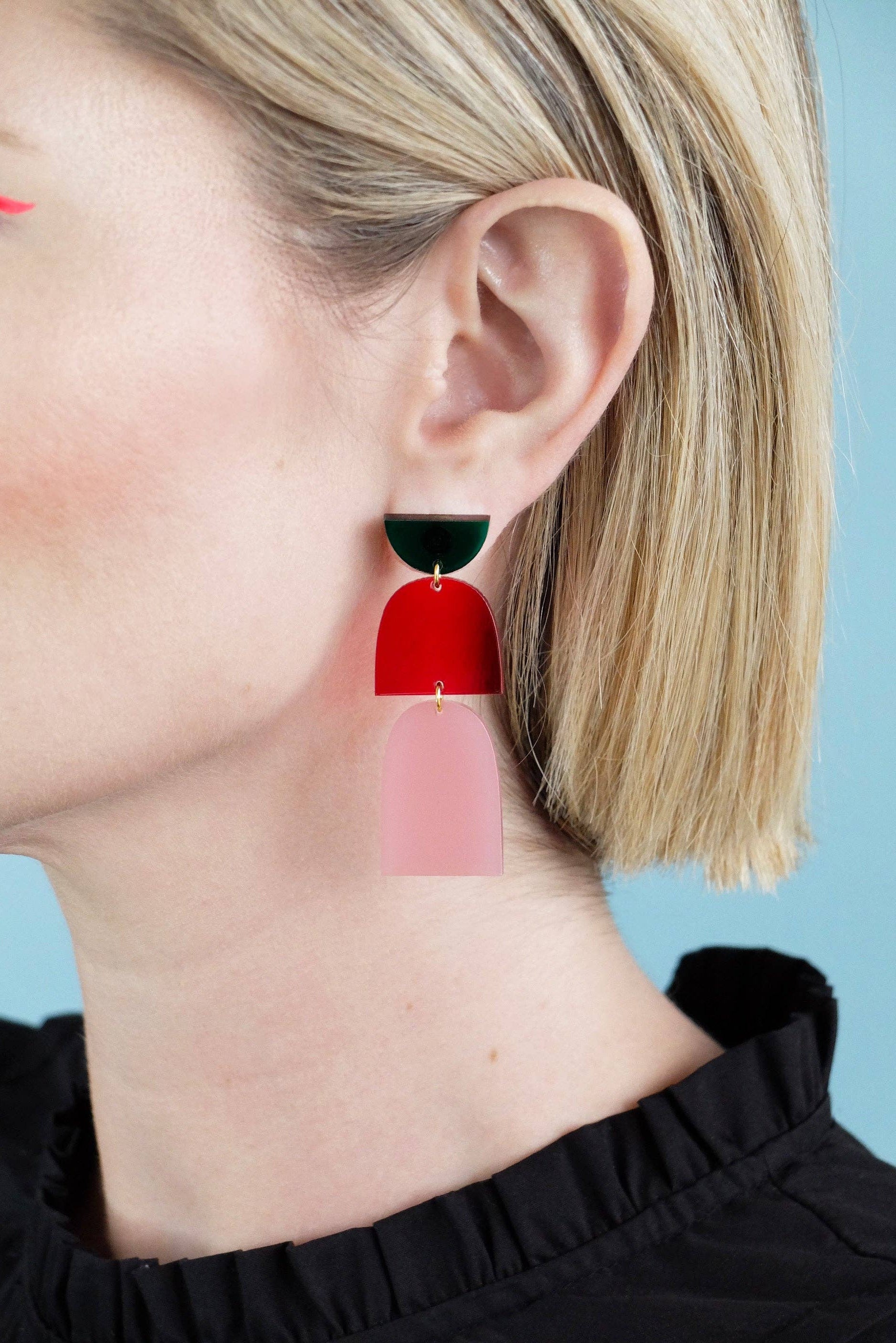 Close-up of a person wearing a red and black earring against a light blue background